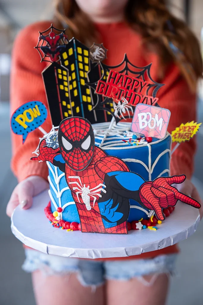Spiderman-Inspired Superhero Blue Birthday Cake Blue 1-tier soft icing birthday cake with a Spiderman cutout, cityscape backdrop, and piped web details