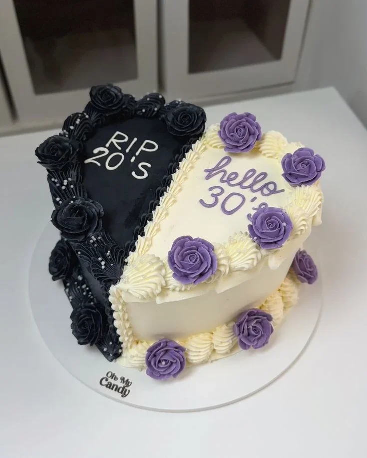 Split Heart Birthday Floral Cake White heart cake with smooth soft icing, black and purple piped floral borders, and scattered white pearl sprinkles