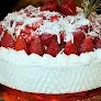White soft-icing cake topped with fresh strawberries and shredded coconut flakes with a textured side design.