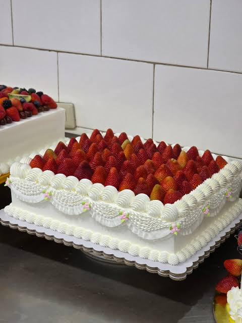 Rectangular white cream cake topped with a dense layer of fresh strawberries and decorated with elegant white icing swags and pink rosettes. Rectangular white cream cake topped with a dense layer of fresh strawberries and decorated with elegant white icing swags and pink rosettes.