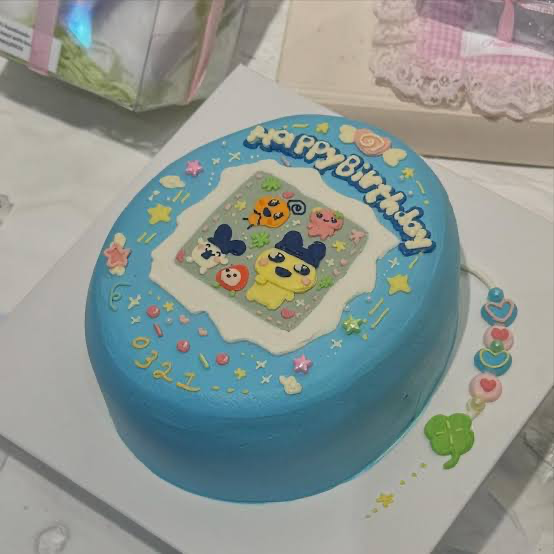 Blue minimalist birthday cake with Tamagotchi character printout and colorful icing doodles. Blue minimalist birthday cake with Tamagotchi character printout and colorful icing doodles.