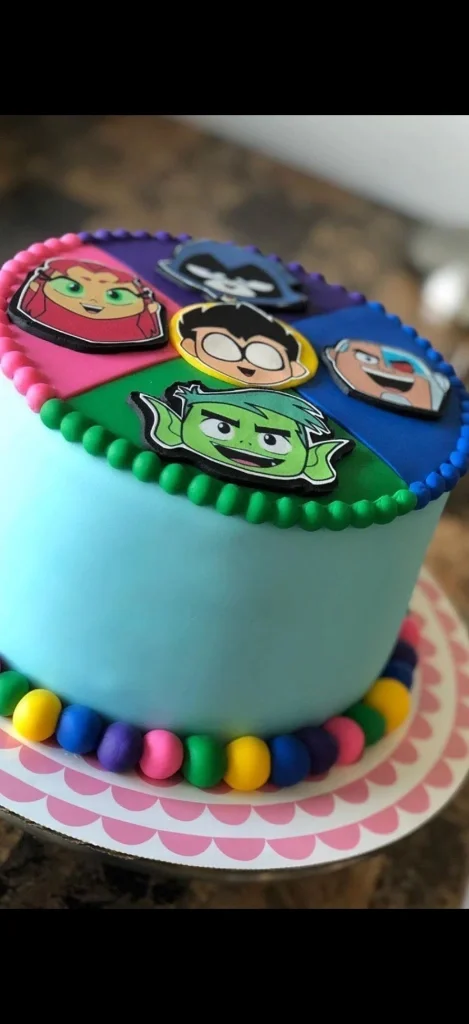 Teen Titans Go themed light blue fondant cake with character face toppers and colorful fondant ball border. Teen Titans Go themed light blue fondant cake with character face toppers and colorful fondant ball border.