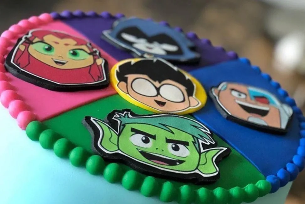 Teen Titans Go themed cake with fondant character faces of Starfire, Raven, Robin, Cyborg, and Beast Boy on a colorful segmented top. Teen Titans Go themed cake with fondant character faces of Starfire, Raven, Robin, Cyborg, and Beast Boy on a colorful segmented top.