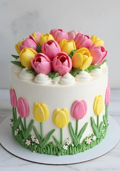 White single tier cake decorated with pink and yellow piped icing tulips on top and around the sides with green leaves and grass. White single tier cake decorated with pink and yellow piped icing tulips on top and around the sides with green leaves and grass.