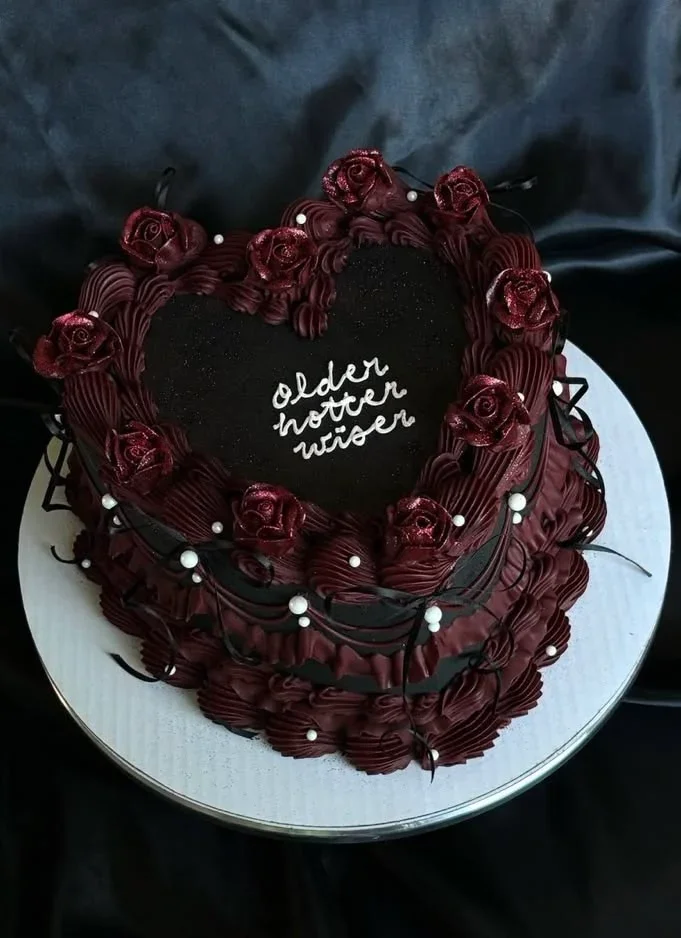 Heart-shaped black vintage cake with dark red icing rosettes, glittery roses, and white pearl accents featuring a handwritten message. Heart-shaped black vintage cake with dark red icing rosettes, glittery roses, and white pearl accents featuring a handwritten message.