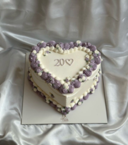 Heart-shaped vintage cake with ivory icing and purple piped rosettes and borders.