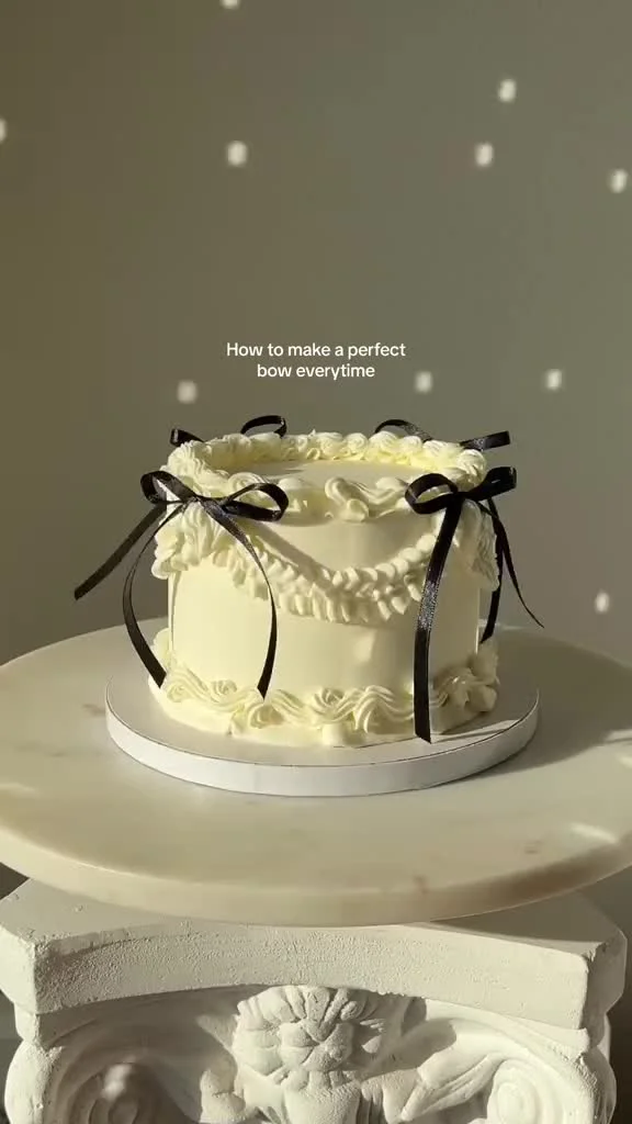Elegant cream-colored minimalist cake with vintage-style piped ruffles and delicate black satin bows.