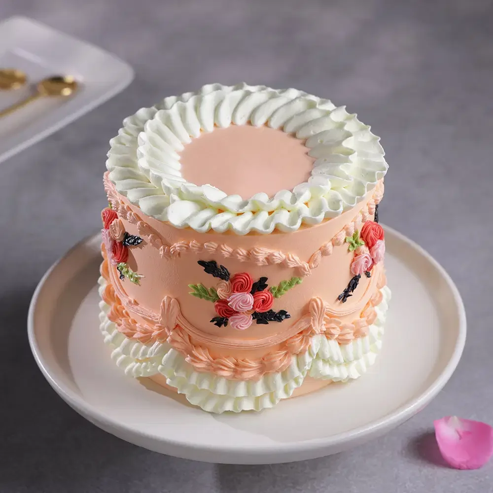 Elegant peach-colored vintage cake with intricate white ruffles and hand-piped pink and red floral icing decorations.