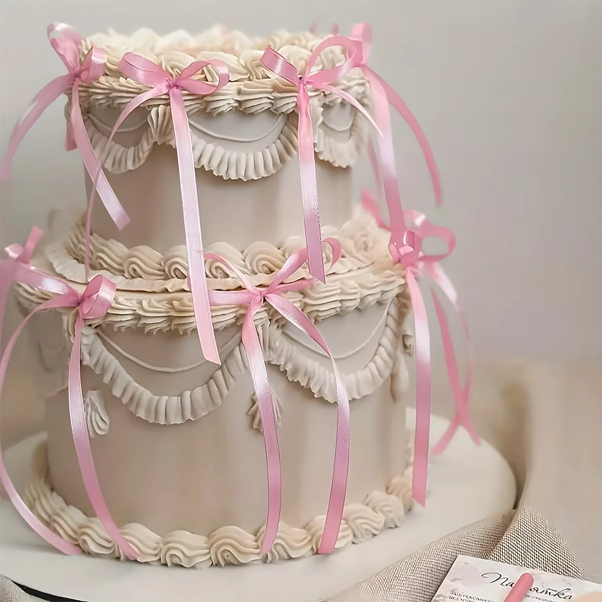 Vintage Ribbon Ivory 2-Tier Cake Ivory 2-tier cake with soft icing, piped swags, and draped pink satin ribbons