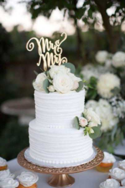 Elegant 2-tier white wedding cake with horizontal textured icing, fresh white roses, and a gold Mr & Mrs cake topper. Elegant 2-tier white wedding cake with horizontal textured icing, fresh white roses, and a gold Mr & Mrs cake topper.