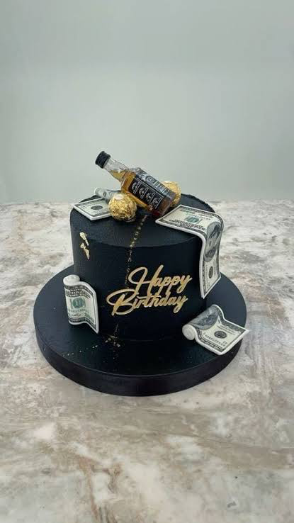 Black 1-tier birthday cake with a whiskey bottle topper, edible dollar bills, and gold Ferrero Rocher chocolates.