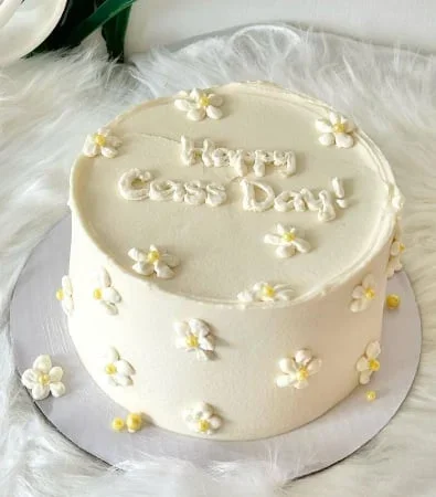 White minimalist birthday cake with piped icing daisies and yellow centers, featuring a 'Happy Cass Day!' message in white icing. White minimalist birthday cake with piped icing daisies and yellow centers, featuring a 'Happy Cass Day!' message in white icing.