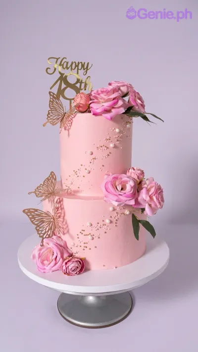 A pink two-tier cake for an 18th birthday, featuring a gold '18th' topper, pink roses, gold butterflies, and white pearls. A pink two-tier cake for an 18th birthday, featuring a gold '18th' topper, pink roses, gold butterflies, and white pearls.