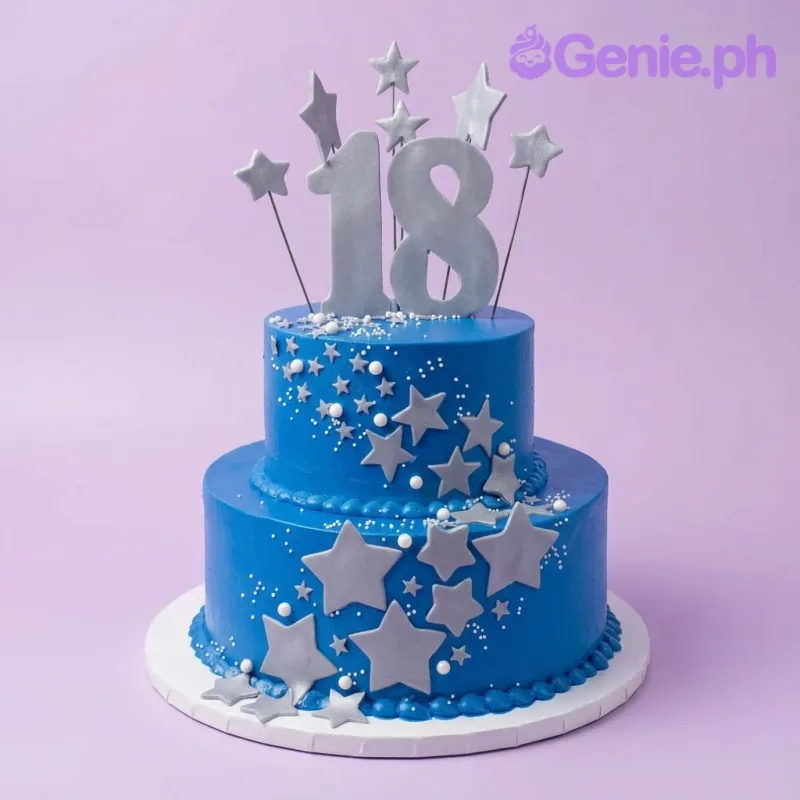 A blue two-tier cake themed for an 18th Birthday, featuring a large silver '18' topper, silver stars, and white pearls. A blue two-tier cake themed for an 18th Birthday, featuring a large silver '18' topper, silver stars, and white pearls.