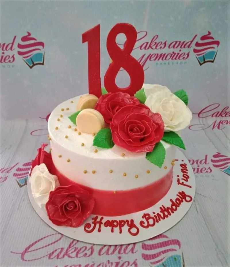 White and red 18th birthday cake with red and white edible roses, gold dragees, and a large red number 18 topper. White and red 18th birthday cake with red and white edible roses, gold dragees, and a large red number 18 topper.