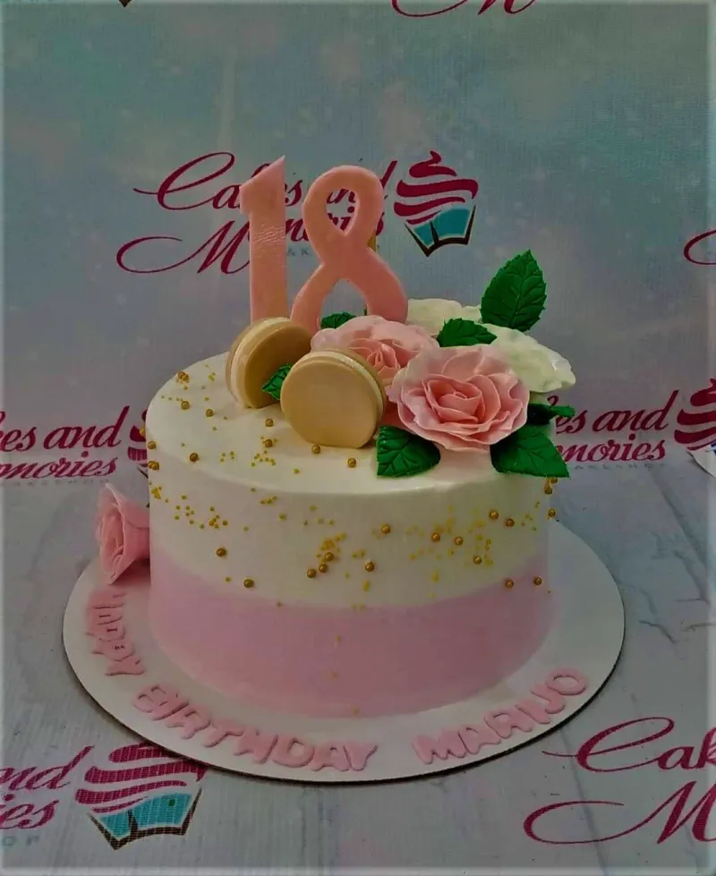 A pink and white ombre 1-tier 18th birthday cake, featuring a pink number 18 topper, roses, macarons, and gold dragees. A pink and white ombre 1-tier 18th birthday cake, featuring a pink number 18 topper, roses, macarons, and gold dragees.