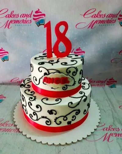 A white, black, and red two-tier 18th Birthday cake, featuring a number 18 topper, black swirls, and red ribbon. A white, black, and red two-tier 18th Birthday cake, featuring a number 18 topper, black swirls, and red ribbon.