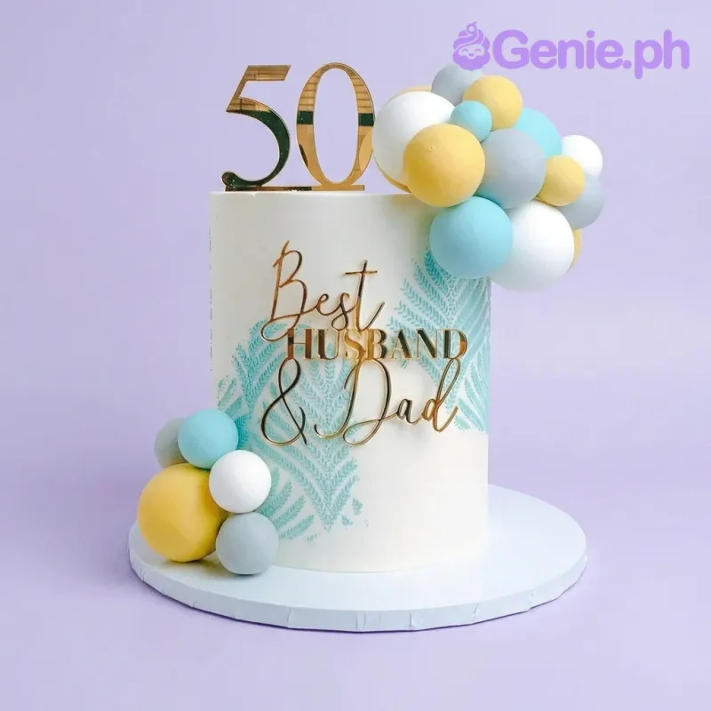 Tall white 50th birthday cake for husband and dad with gold acrylic toppers and blue, yellow, and grey balloon clusters. Tall white 50th birthday cake for husband and dad with gold acrylic toppers and blue, yellow, and grey balloon clusters.