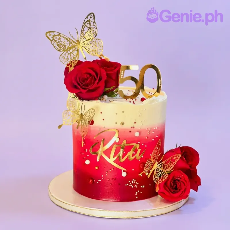 A tall 1-tier cake with a red and white gradient icing, decorated with red fresh roses, gold butterfly cutouts, and a gold '50 Rita' topper. A tall 1-tier cake with a red and white gradient icing, decorated with red fresh roses, gold butterfly cutouts, and a gold '50 Rita' topper.