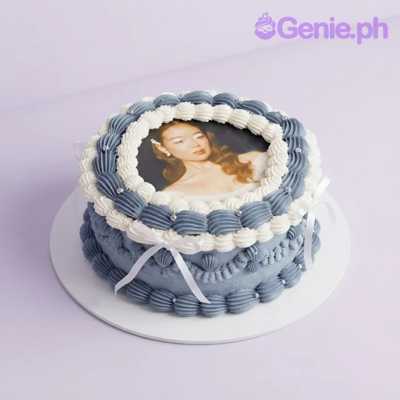 White 1-tier cake with a portrait photo top, navy piped icing border, silver pearls, and white ribbon bows White 1-tier cake with a portrait photo top, navy piped icing border, silver pearls, and white ribbon bows