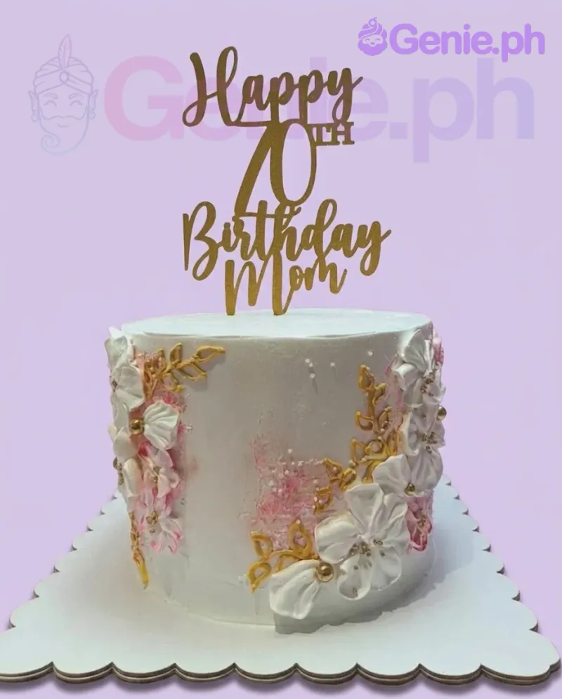 A white 1-tier cake themed '70th Birthday Mom', featuring a gold glitter topper, white icing flowers, and gold leaves. A white 1-tier cake themed '70th Birthday Mom', featuring a gold glitter topper, white icing flowers, and gold leaves.