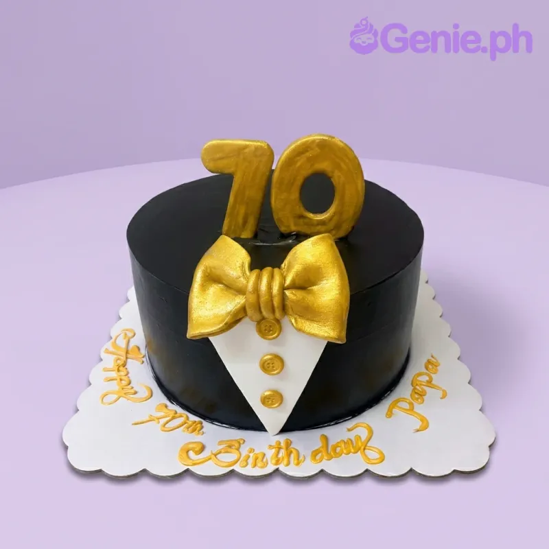 A black, white, and gold 1-tier fondant cake, tuxedo-themed, with gold '70' numbers, a gold bow tie, and a white shirt panel. A black, white, and gold 1-tier fondant cake, tuxedo-themed, with gold '70' numbers, a gold bow tie, and a white shirt panel.