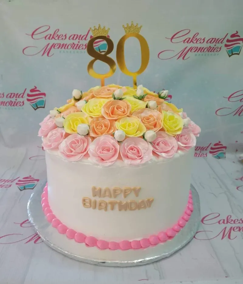 A white 1-tier 80th birthday cake with gold 80 toppers and a dome of pink, yellow, peach icing roses. A white 1-tier 80th birthday cake with gold 80 toppers and a dome of pink, yellow, peach icing roses.