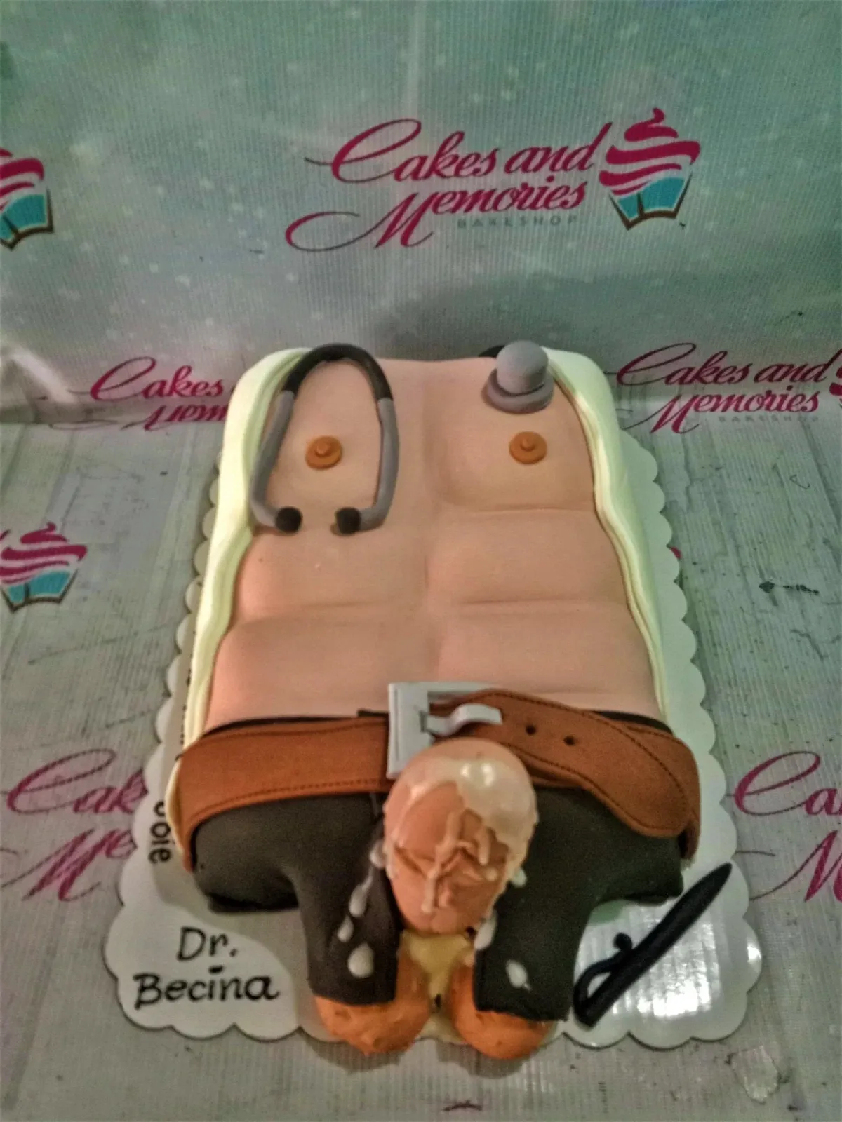 A peach and white rectangle fondant cake shaped as a muscular male torso, featuring a stethoscope and a small figure. A peach and white rectangle fondant cake shaped as a muscular male torso, featuring a stethoscope and a small figure.