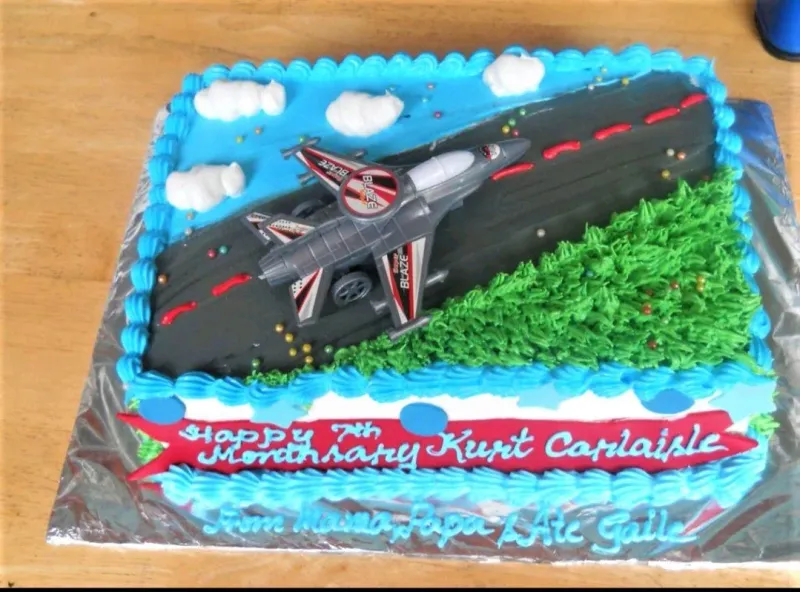 A rectangular blue and green airplane themed cake with a toy jet on a runway and piped clouds. A rectangular blue and green airplane themed cake with a toy jet on a runway and piped clouds.