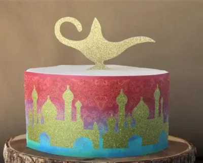 A white and gold 1-tier cake themed around Aladdin, featuring a gold glitter magic lamp topper and a colorful palace silhouette panel. A white and gold 1-tier cake themed around Aladdin, featuring a gold glitter magic lamp topper and a colorful palace silhouette panel.