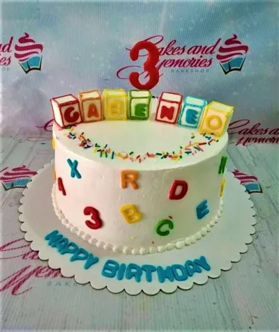 A white 1-tier cake themed around Alphabet Blocks, featuring a red number 3, colorful alphabet blocks, and scattered letters with rainbow sprinkles. A white 1-tier cake themed around Alphabet Blocks, featuring a red number 3, colorful alphabet blocks, and scattered letters with rainbow sprinkles.