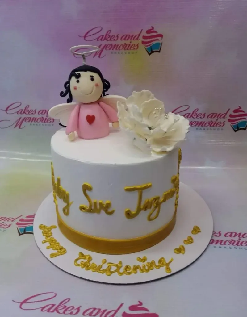 White 1-tier christening cake with a pink angel fondant figure, a large white sugar flower, and gold icing text. White 1-tier christening cake with a pink angel fondant figure, a large white sugar flower, and gold icing text.
