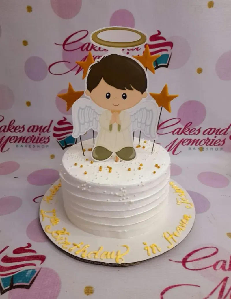 White 1-tier angel birthday cake with a boy angel printout topper, gold stars, and gold dragees on a white soft-icing base. White 1-tier angel birthday cake with a boy angel printout topper, gold stars, and gold dragees on a white soft-icing base.