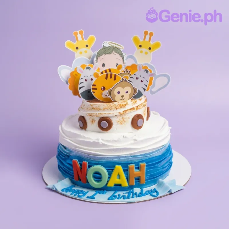 A blue and white 1 Tier cake themed around a safari, featuring animal printouts, gumpaste 'NOAH' letters, and a 'Happy 1st birthday' banner. A blue and white 1 Tier cake themed around a safari, featuring animal printouts, gumpaste 'NOAH' letters, and a 'Happy 1st birthday' banner.