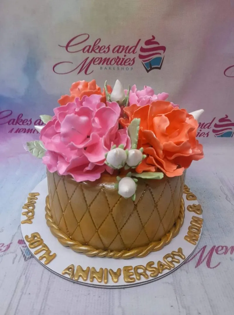 A gold quilted fondant Anniversary cake with large pink and orange flowers, a gold rope border, and text. A gold quilted fondant Anniversary cake with large pink and orange flowers, a gold rope border, and text.