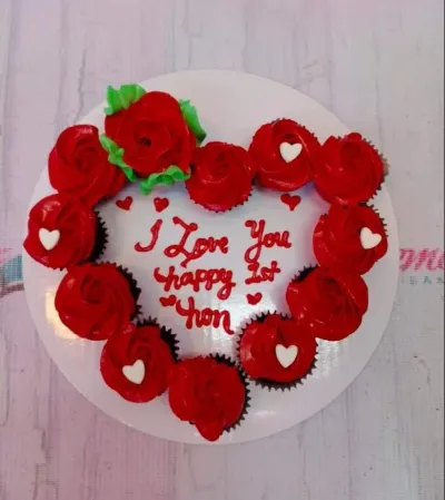 A white and red heart-shaped pull-apart cupcake, themed for an anniversary, adorned with red icing roses, white heart accents, and red text. A white and red heart-shaped pull-apart cupcake, themed for an anniversary, adorned with red icing roses, white heart accents, and red text.