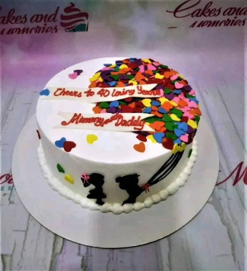 A white 1-tier cake themed around Anniversary, featuring colorful heart confetti and black silhouettes of a couple. A white 1-tier cake themed around Anniversary, featuring colorful heart confetti and black silhouettes of a couple.