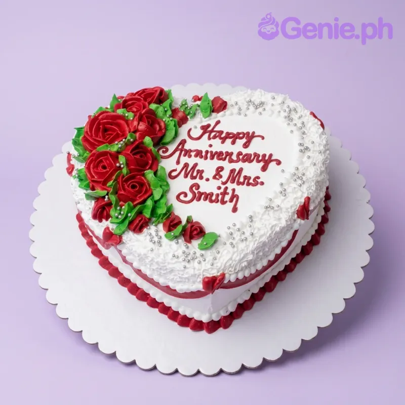 Heart-shaped white anniversary cake with red icing roses, green leaves, silver dragees, and a personalized message. Heart-shaped white anniversary cake with red icing roses, green leaves, silver dragees, and a personalized message.