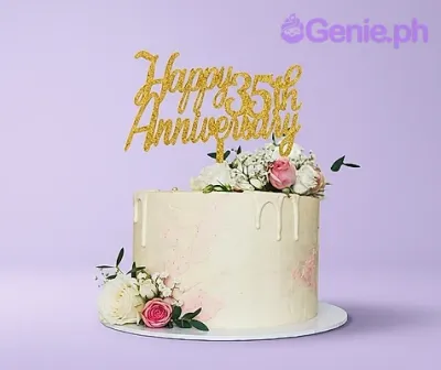 A white 1-tier anniversary cake with white drips, white and pink roses, and a gold glitter 35th anniversary topper. A white 1-tier anniversary cake with white drips, white and pink roses, and a gold glitter 35th anniversary topper.