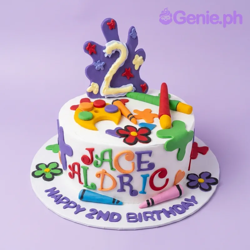 White round art-themed birthday cake with colorful fondant paint splats, crayons, and a paint palette. White round art-themed birthday cake with colorful fondant paint splats, crayons, and a paint palette.
