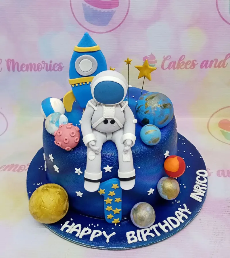 A dark blue 1-tier fondant cake themed around Astronaut Space, featuring a fondant astronaut, rocket, colorful planets, and stars. A dark blue 1-tier fondant cake themed around Astronaut Space, featuring a fondant astronaut, rocket, colorful planets, and stars.