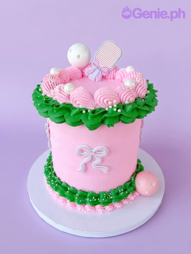 A pink, green, and white 1 Tier cake themed around a baby rattle, featuring a pink striped rattle printout and green ruffle icing. A pink, green, and white 1 Tier cake themed around a baby rattle, featuring a pink striped rattle printout and green ruffle icing.