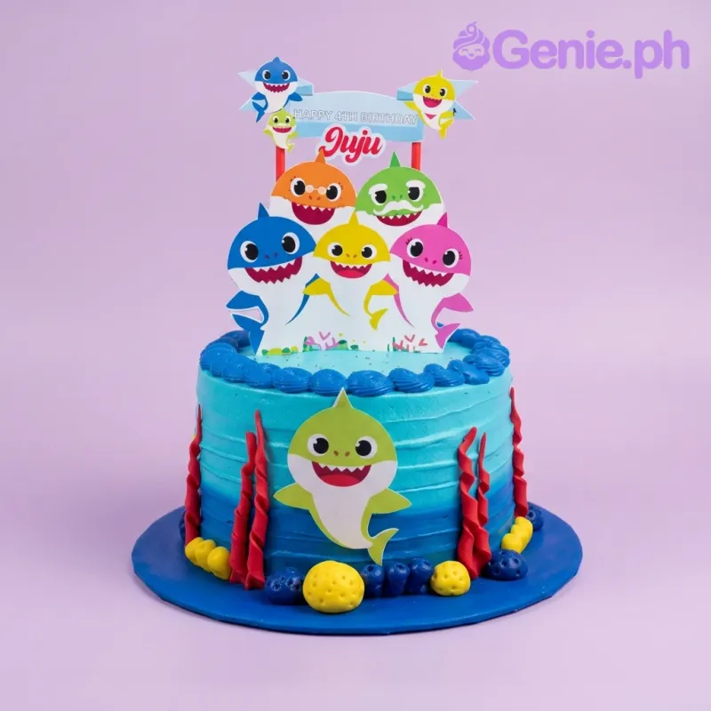 Blue Baby Shark themed birthday cake with colorful shark printouts and red gumpaste coral decorations. Blue Baby Shark themed birthday cake with colorful shark printouts and red gumpaste coral decorations.