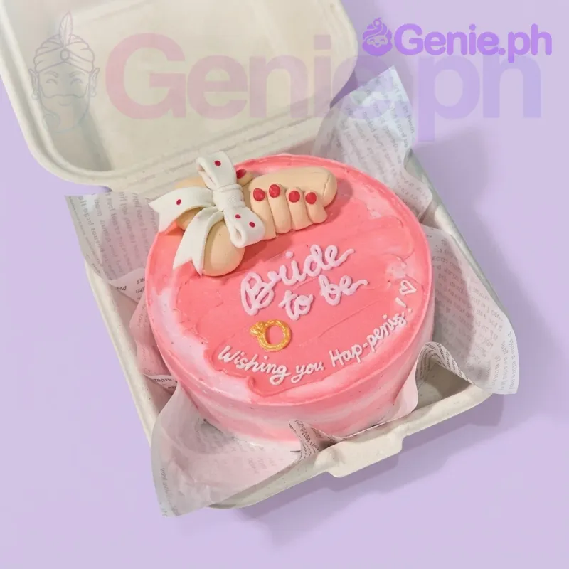A pink and white Bento cake themed around Bachelorette, featuring a 3D fondant hand, a gold ring, and white icing text. A pink and white Bento cake themed around Bachelorette, featuring a 3D fondant hand, a gold ring, and white icing text.