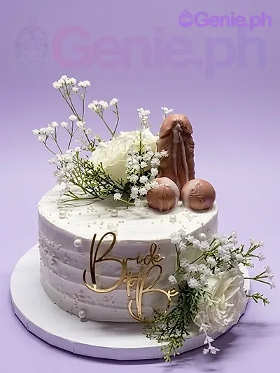 A white 1 Tier Bachelorette cake, featuring a brown phallic-shaped fondant topper, white roses, and baby's breath. A white 1 Tier Bachelorette cake, featuring a brown phallic-shaped fondant topper, white roses, and baby's breath.