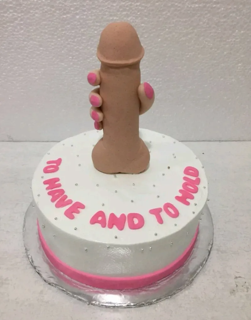 A white 1 Tier Bachelorette cake with a 3D fondant hand holding a phallic shape, pink text, and silver dragees. A white 1 Tier Bachelorette cake with a 3D fondant hand holding a phallic shape, pink text, and silver dragees.