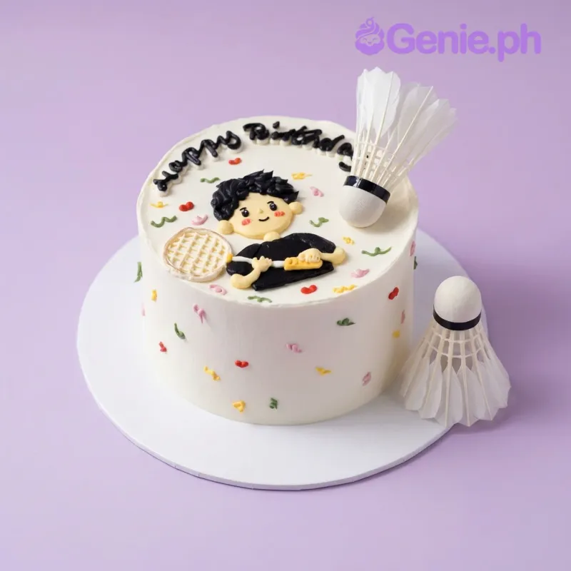 White 1-tier cake with soft icing, a badminton player character, shuttlecocks, a racket, and colorful confetti accents White 1-tier cake with soft icing, a badminton player character, shuttlecocks, a racket, and colorful confetti accents