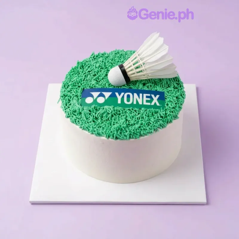 White 1-tier cake with green piped grass icing, a Yonex logo printout, and a plastic badminton shuttlecock topper White 1-tier cake with green piped grass icing, a Yonex logo printout, and a plastic badminton shuttlecock topper