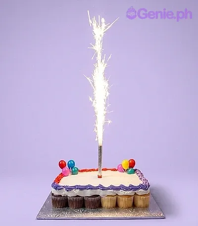 A white rectangular pull-apart cupcake cake with blue and red borders, featuring balloon toppers and a sparkler candle. A white rectangular pull-apart cupcake cake with blue and red borders, featuring balloon toppers and a sparkler candle.