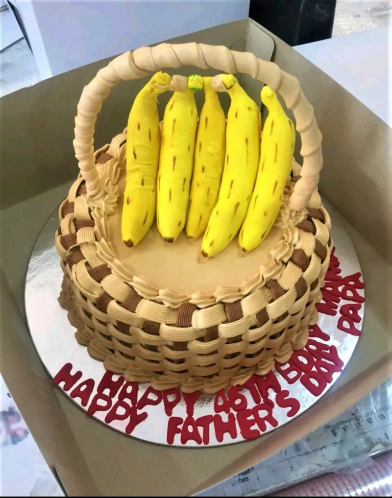 A tan and brown 1-tier Banana Basket cake, featuring five yellow fondant bananas, a gumpaste handle, and a woven icing design. A tan and brown 1-tier Banana Basket cake, featuring five yellow fondant bananas, a gumpaste handle, and a woven icing design.